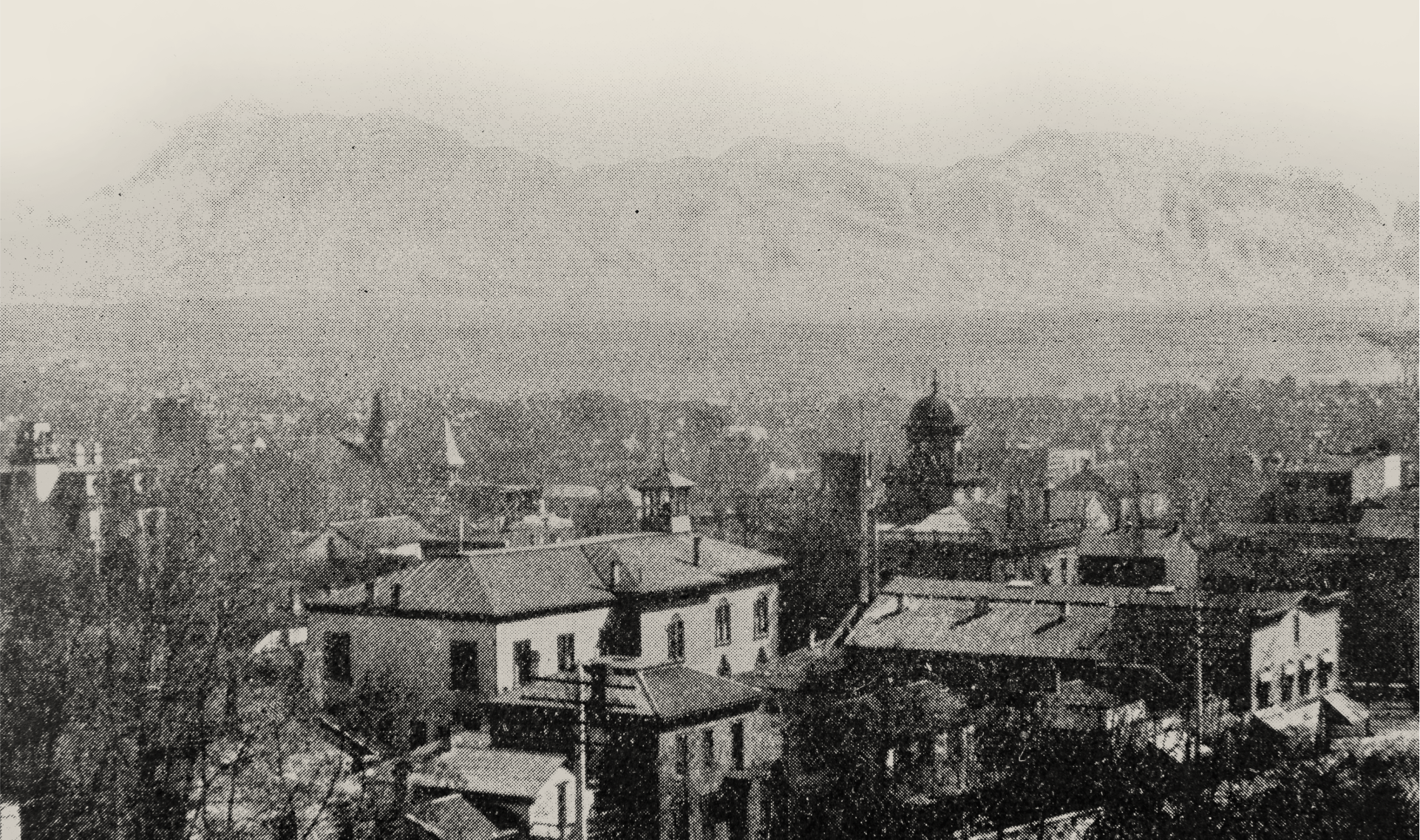 A historical back and white image of a town with mountains in the background