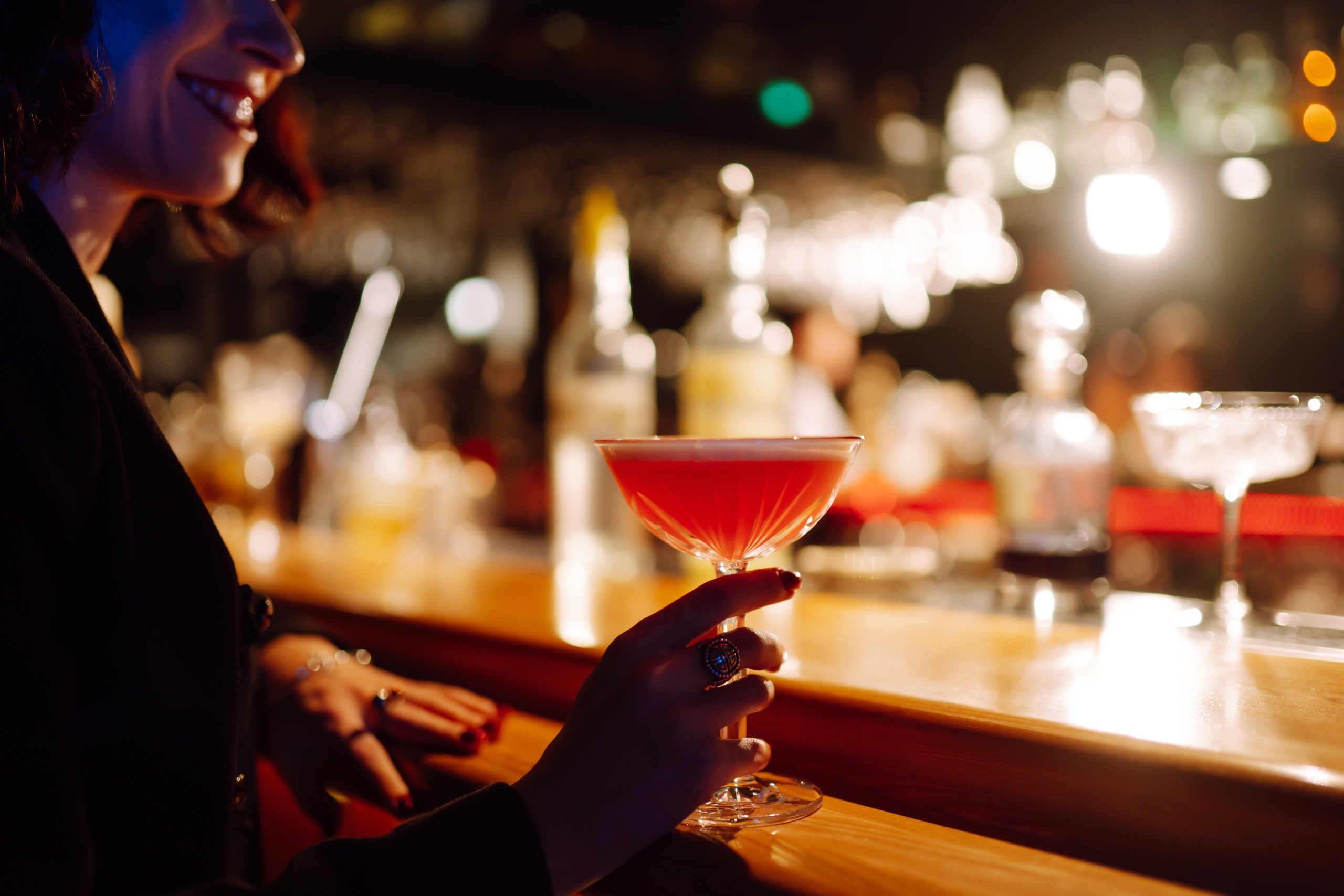 A woman holds a pink cocktail at a moody bar