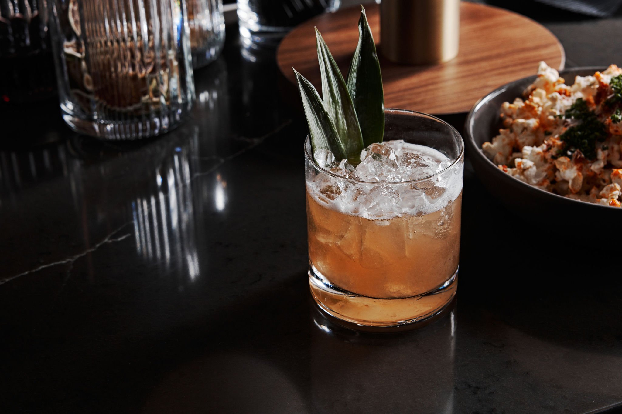 A cocktail garnished with large leaves sitting next to popcorn No. 119 at Asher Adams Hotel, Salt Lake City