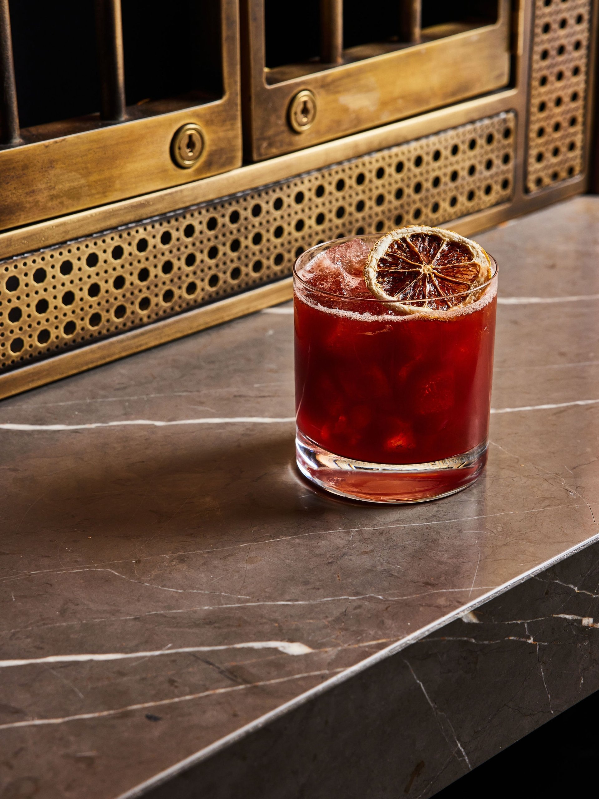 A dark pink cocktail with dried lemon wedge garnish at The Bar at Asher Adams, Salt Lake City