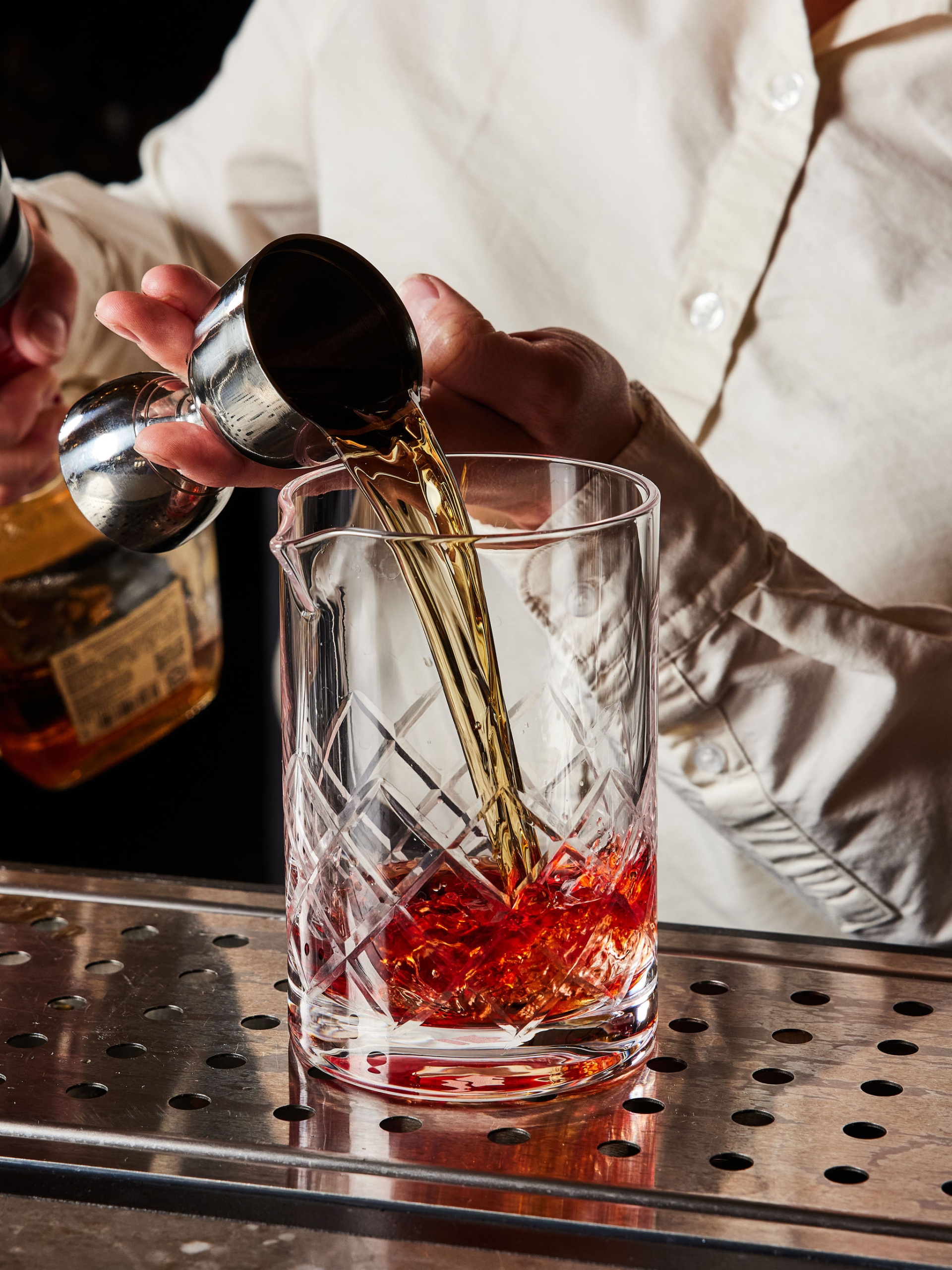 A bar tender pours a shot into a crystal glass at The Bar at Asher Adams, Salt Lake City