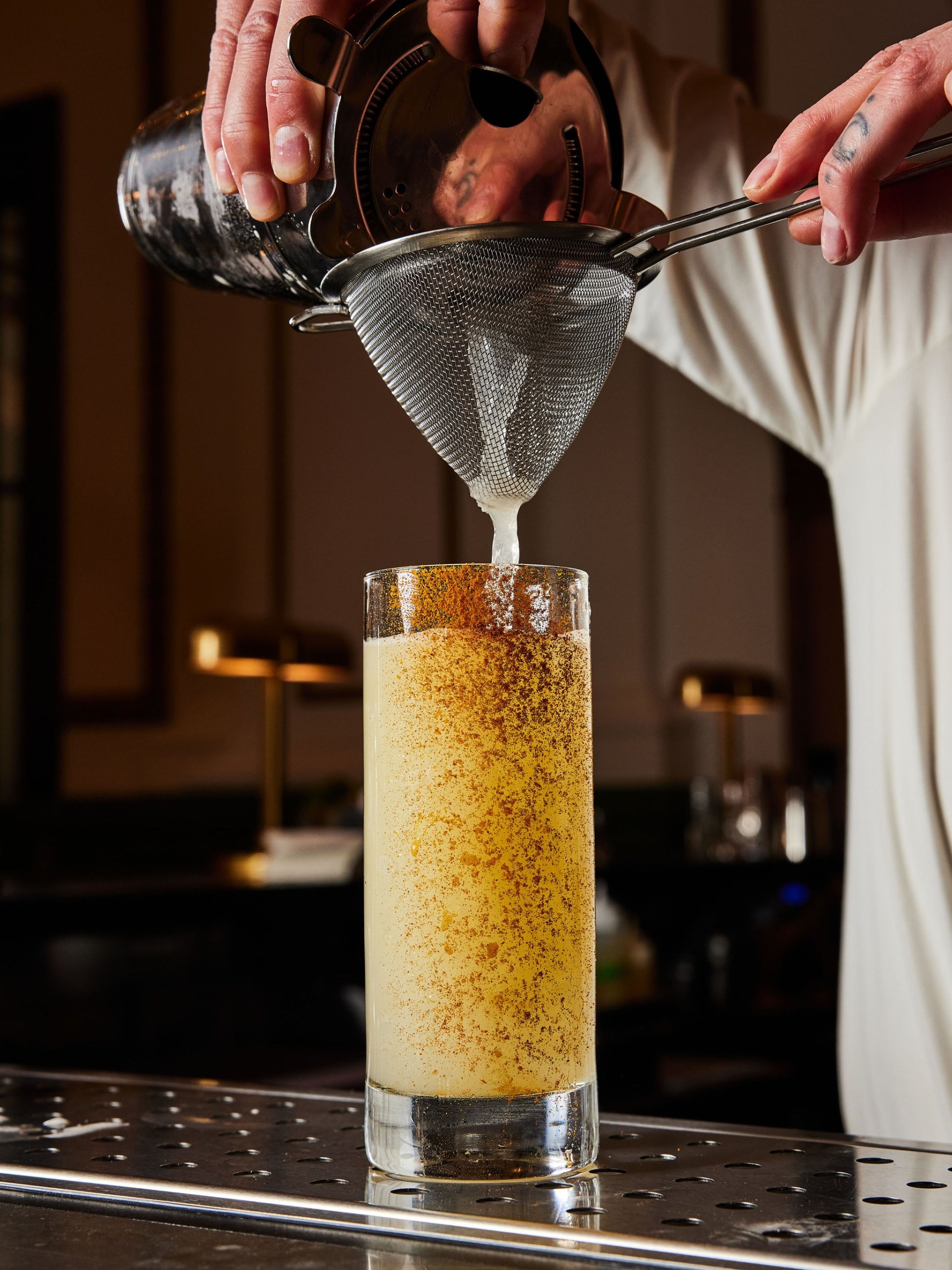 A bartender pours a cocktail through a strainer into a tall rimmed glass at The Bar at Asher Adams, Salt Lake City