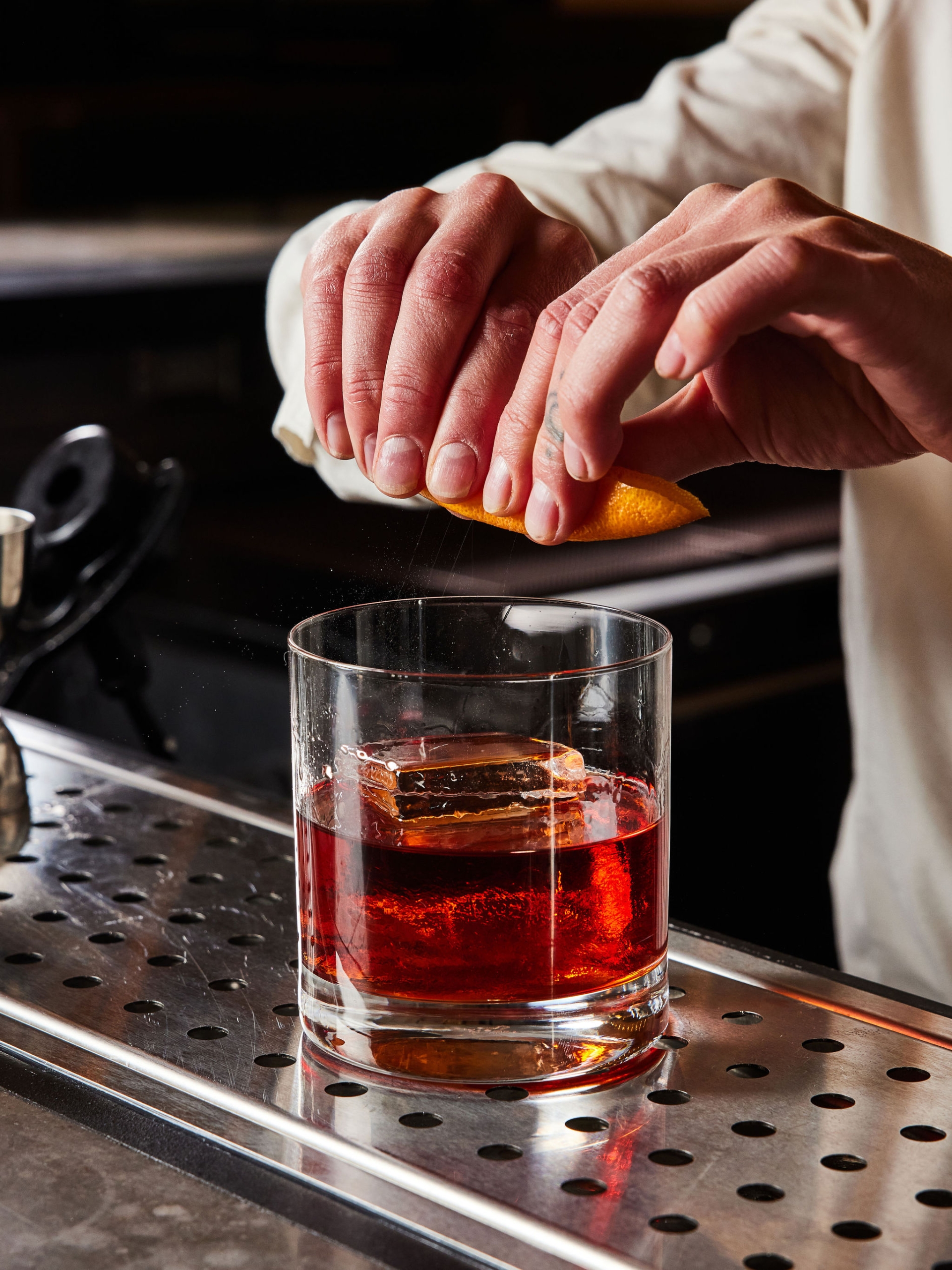 A bar tender squeezes an orange rind over an old fashioned at The Bar at Asher Adams, Salt Lake City