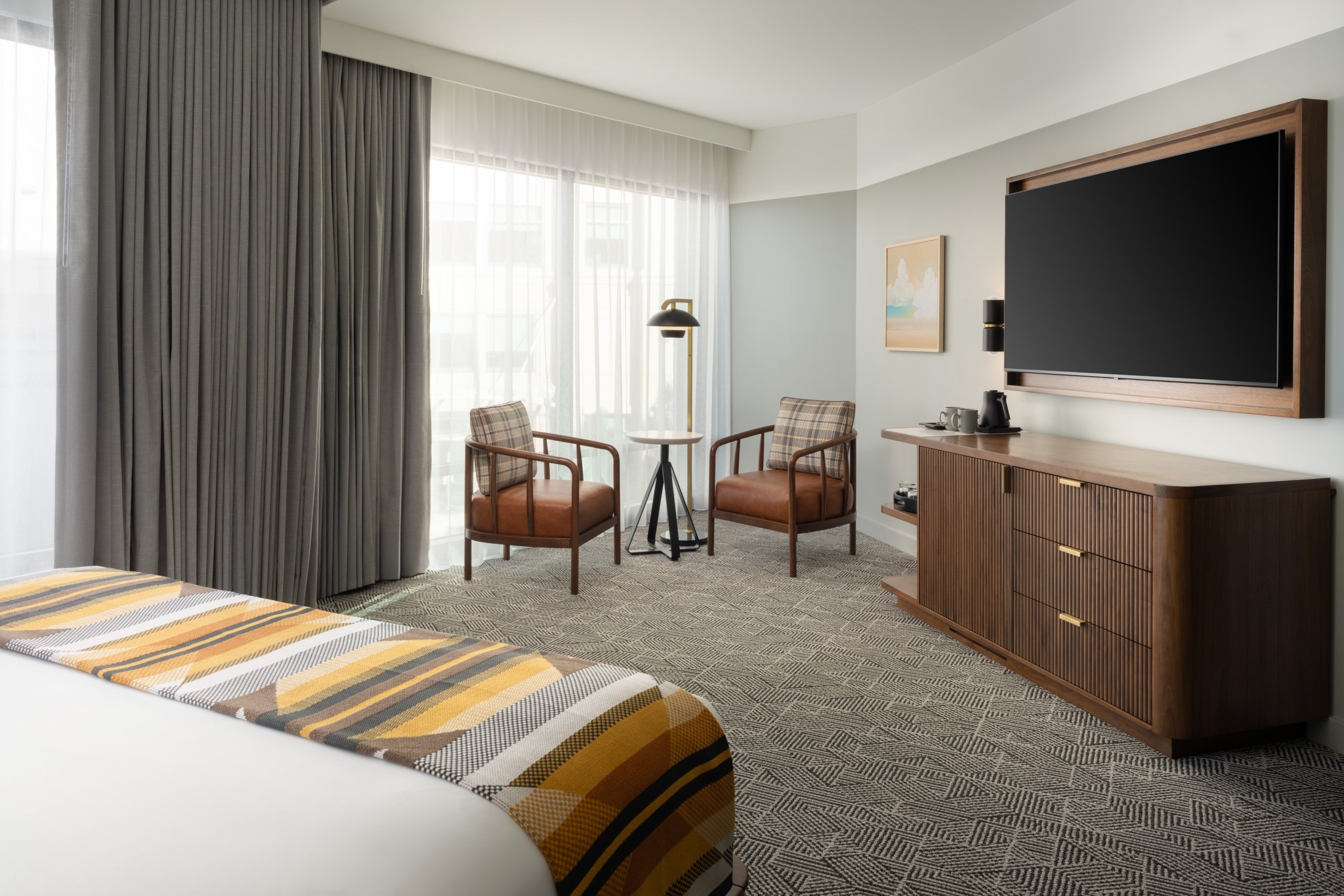 A king bedroom featuring a seating area, wall mounted HGTV and pour over coffee amenities at Asher Adams Hotel, Salt Lake City