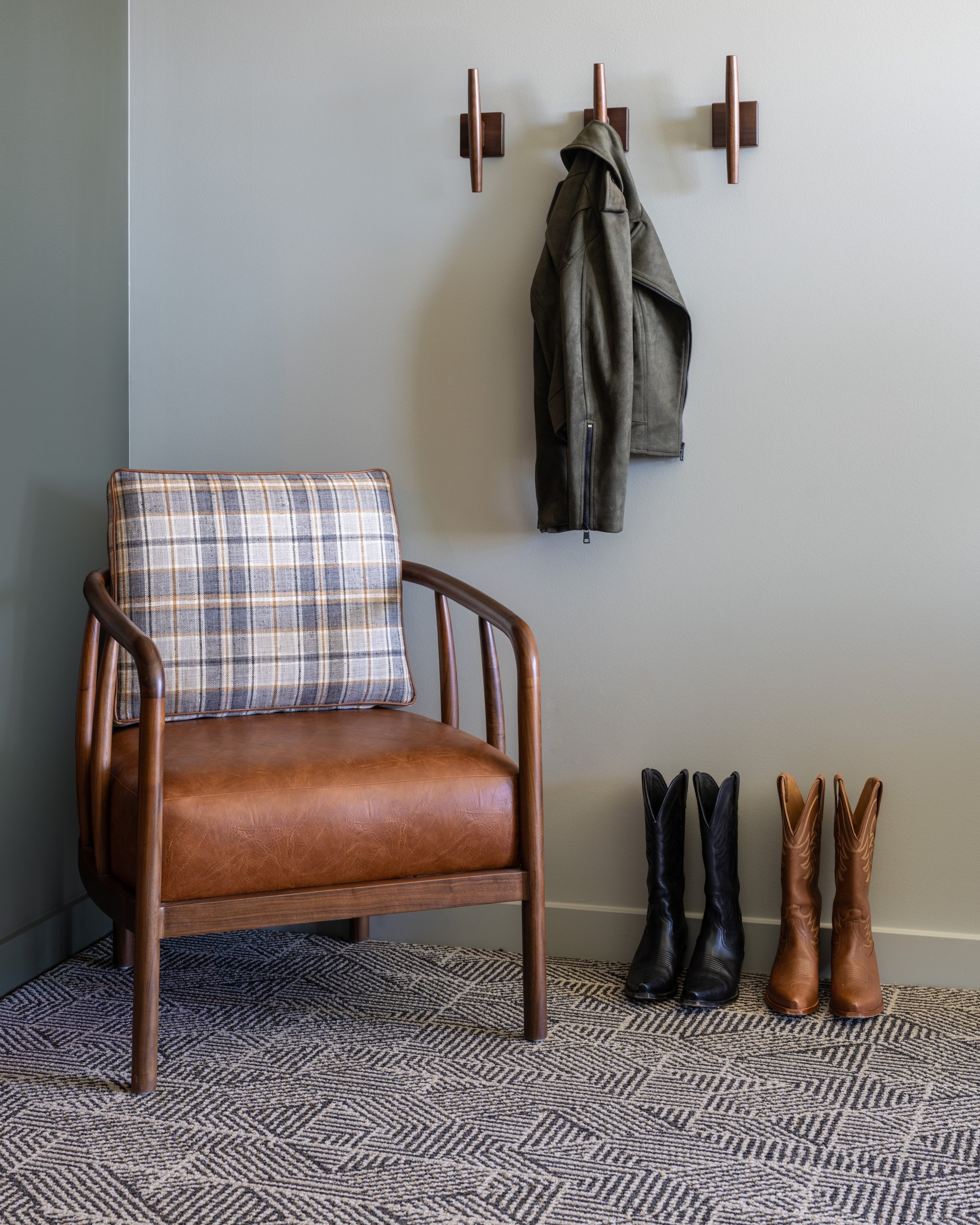 A leather chair next to boots and wall-mounted coat racks