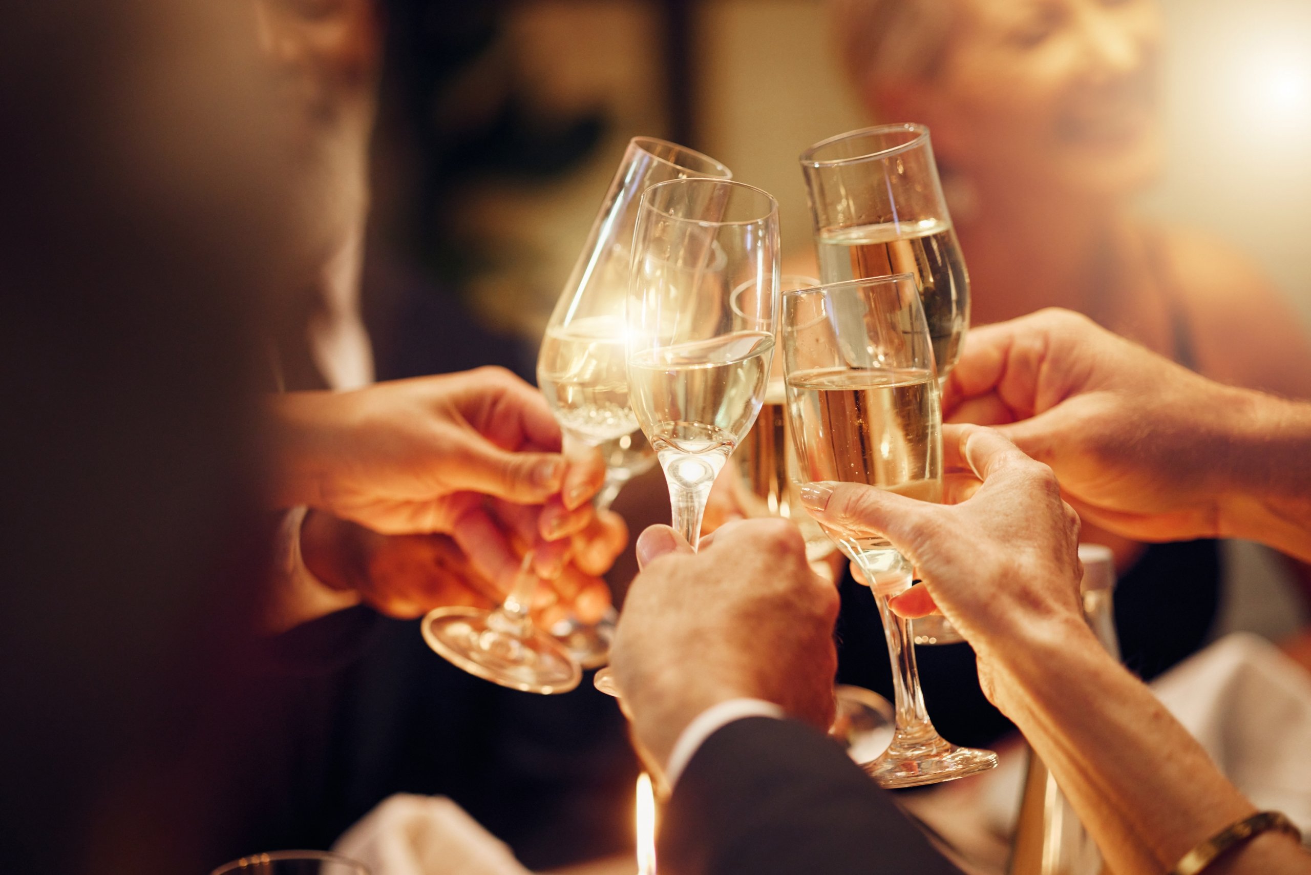 Four hands holding champagne flutes clinking glasses.