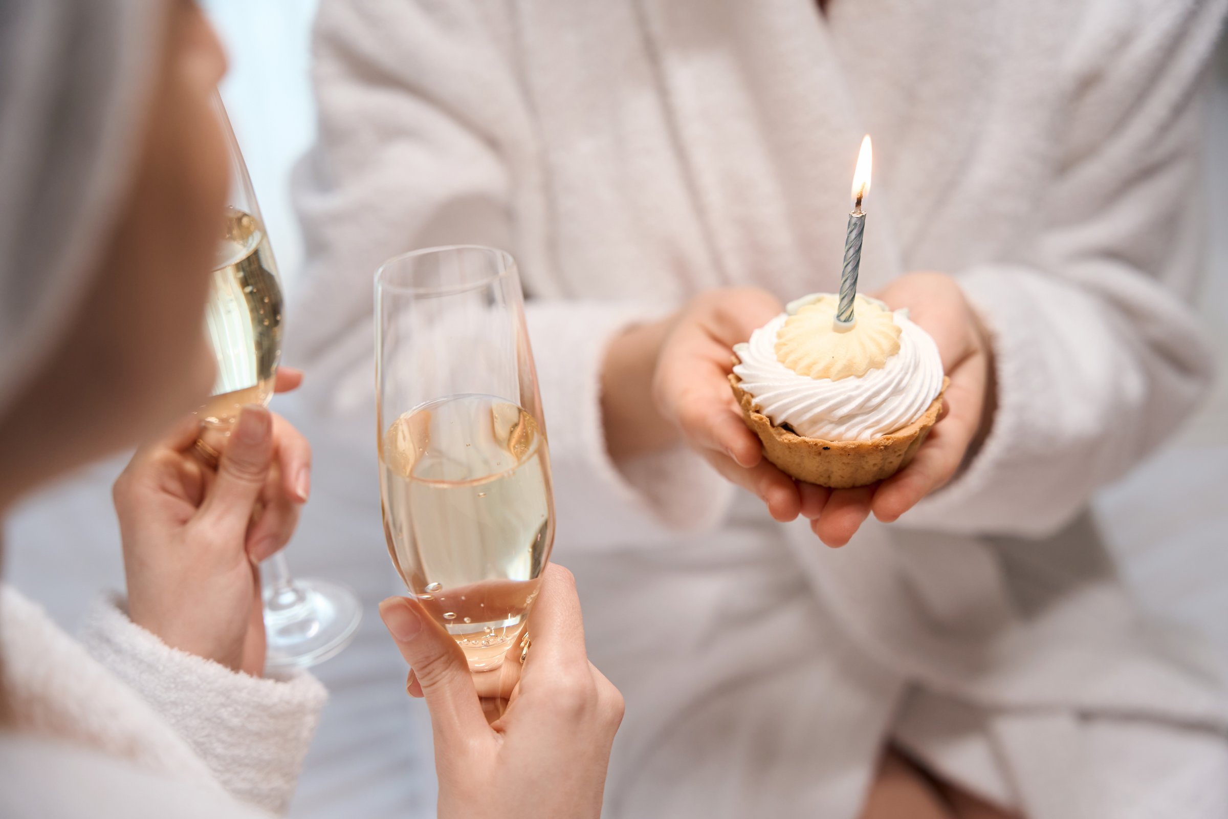 A person holding two glasses of champagne and a person holding a birthday cupcake