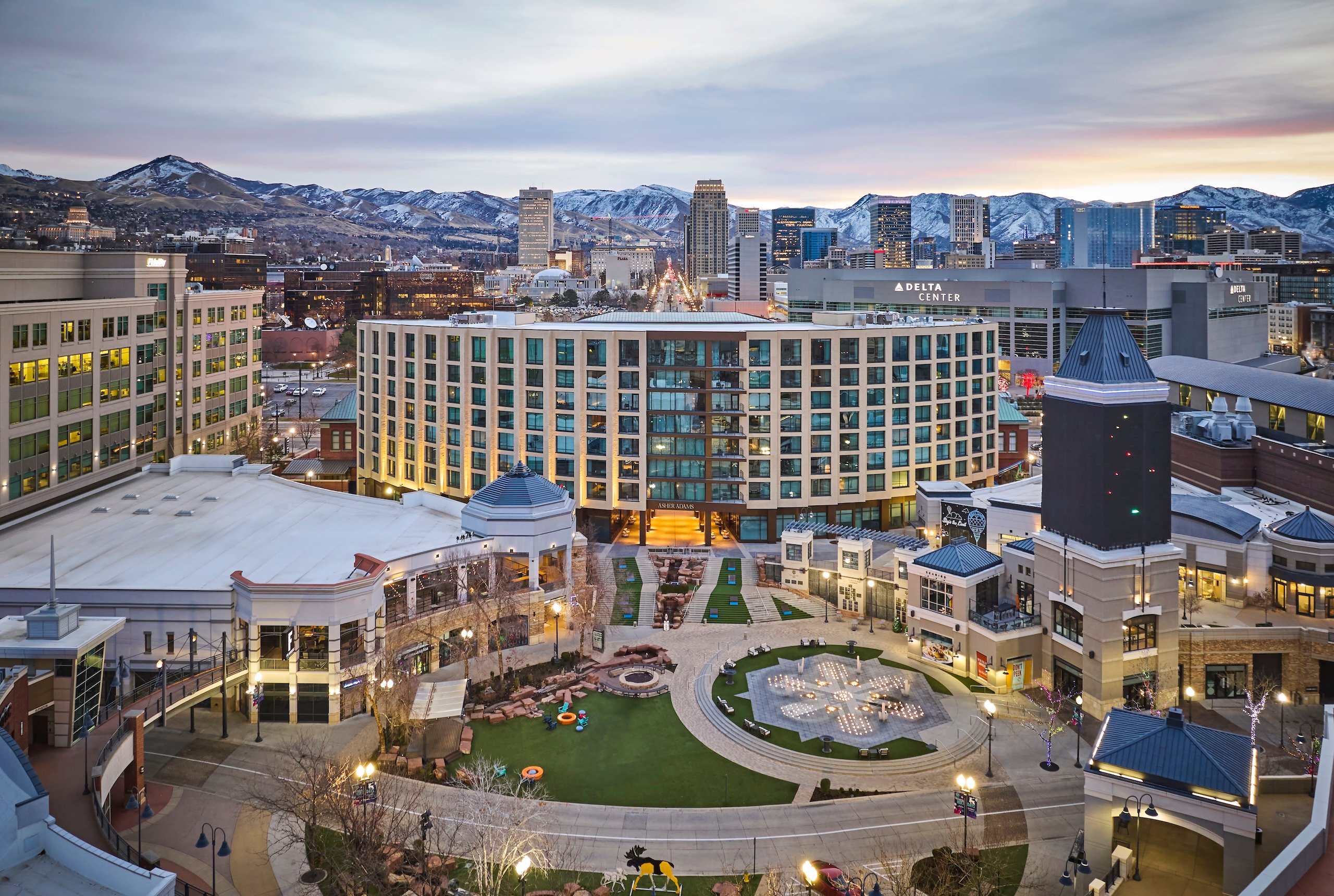 The exterior of Asher Adams hotel, the Delta Center, and Salt Lake City's snow-capped mountains