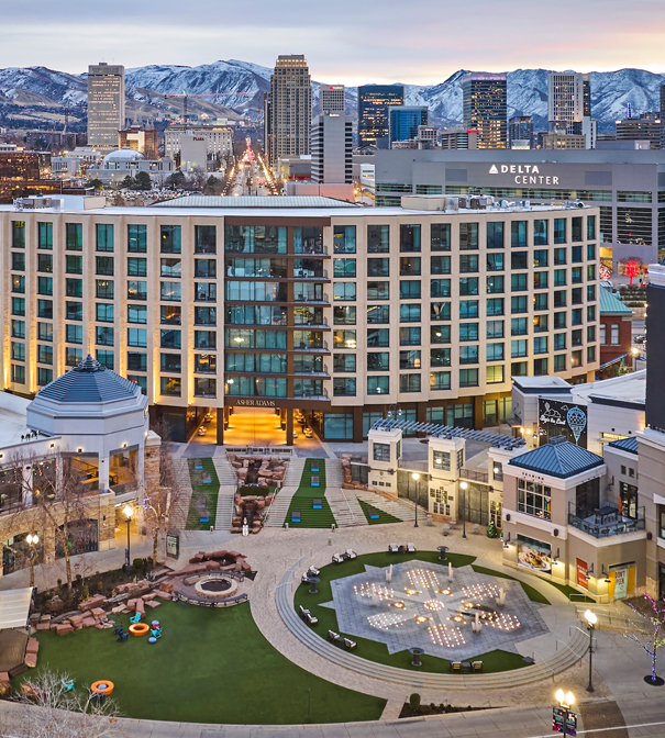 The exterior of Asher Adams Hotel from an aerial view, the city and mountains seen in the background.