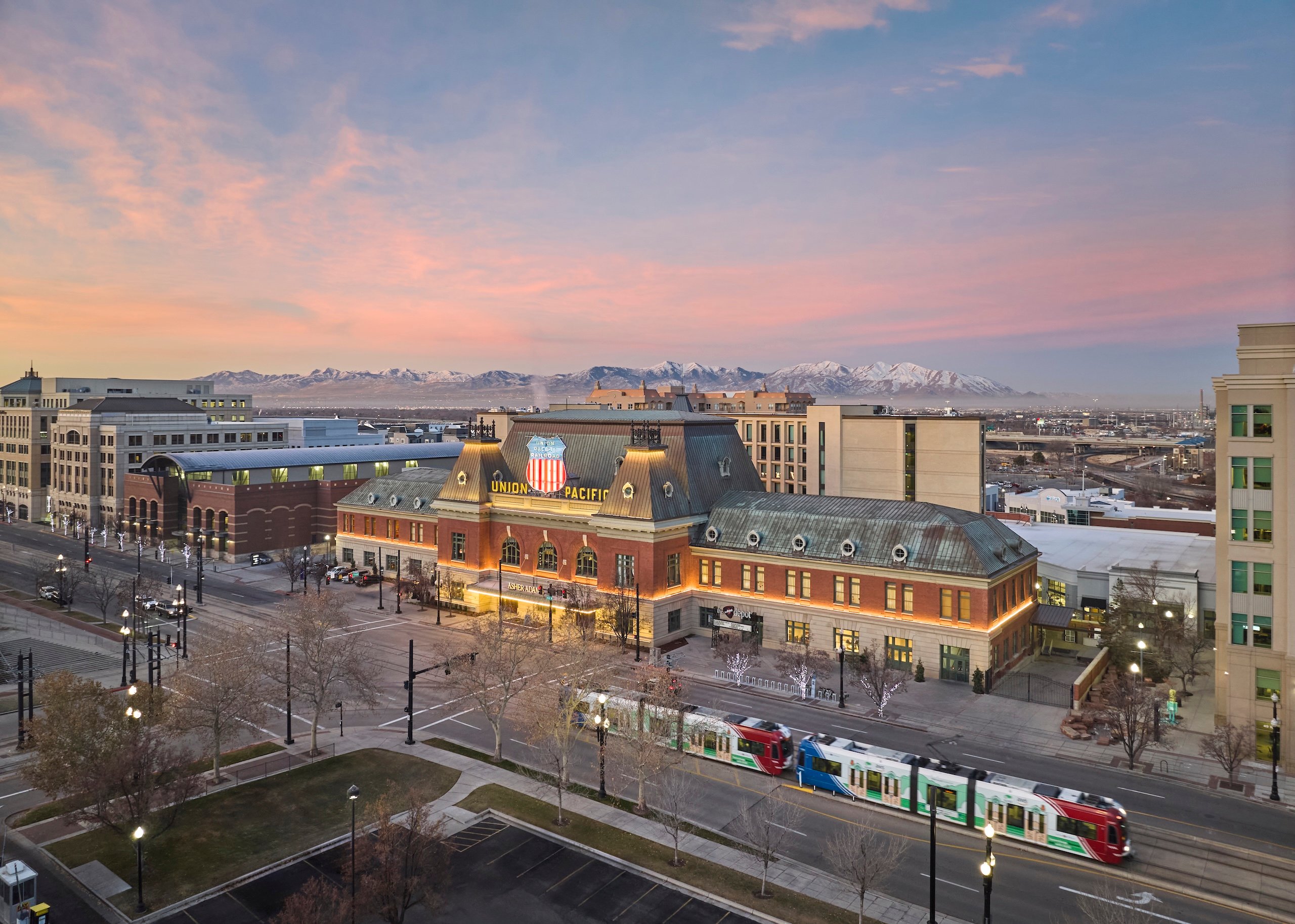 The exterior of Asher Adams Hotel from an aerial view, at sunset, Salt Lake City and mountains in the background.