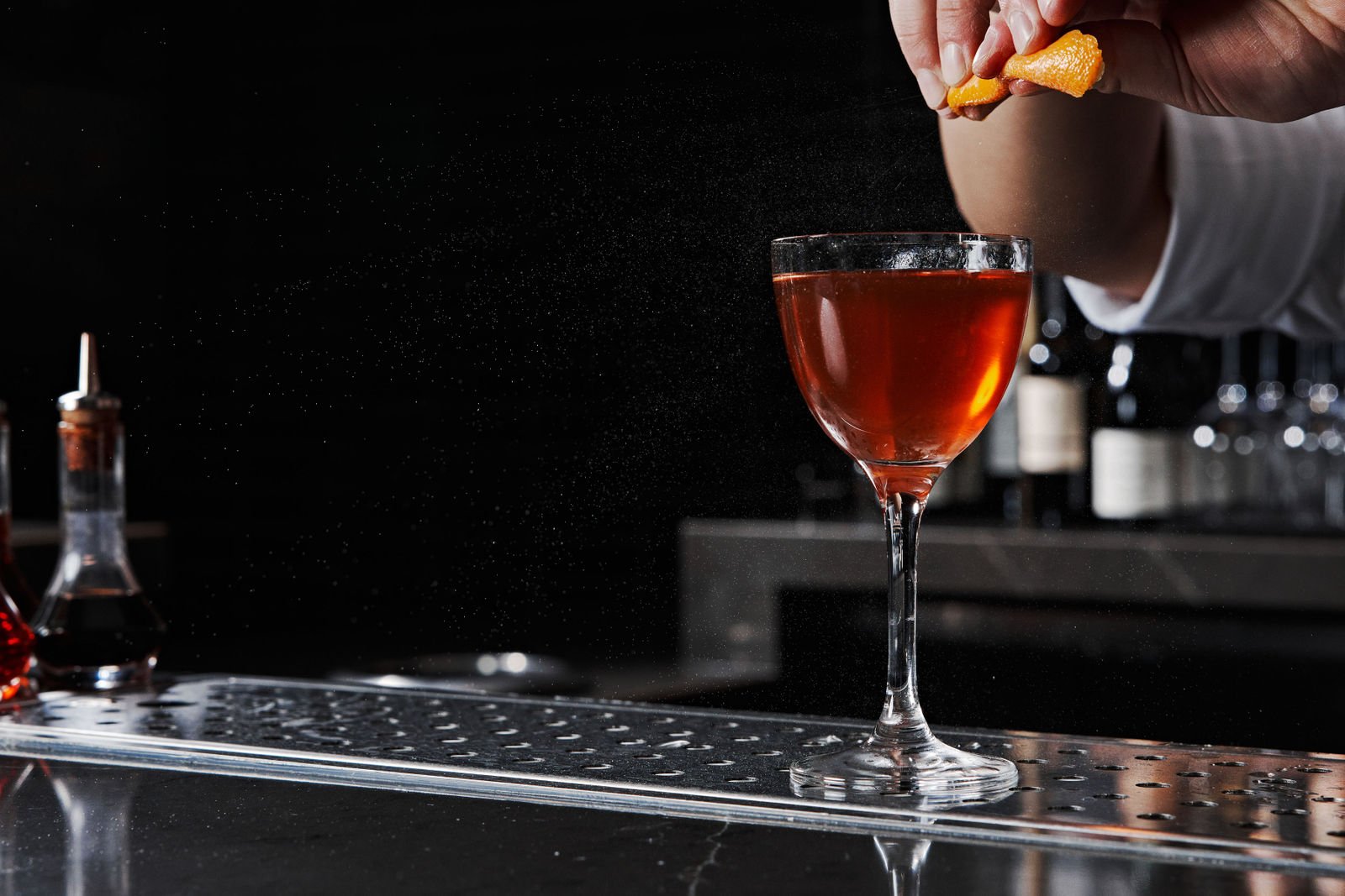 A bartender squeezer orange zest into a red cocktail