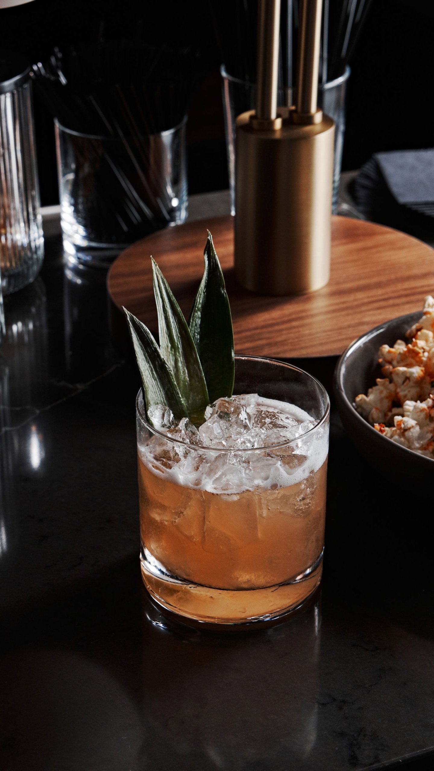 A cocktail on a bar with dark green leaves as garnish