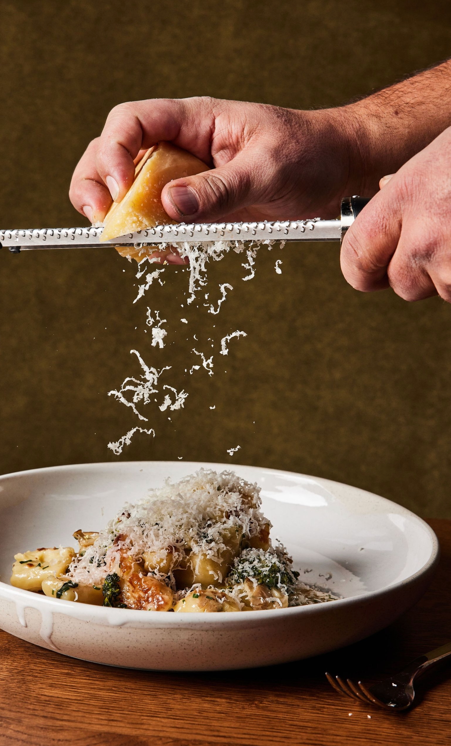 A hand grating parmesan cheese over a bowl of gnocchi