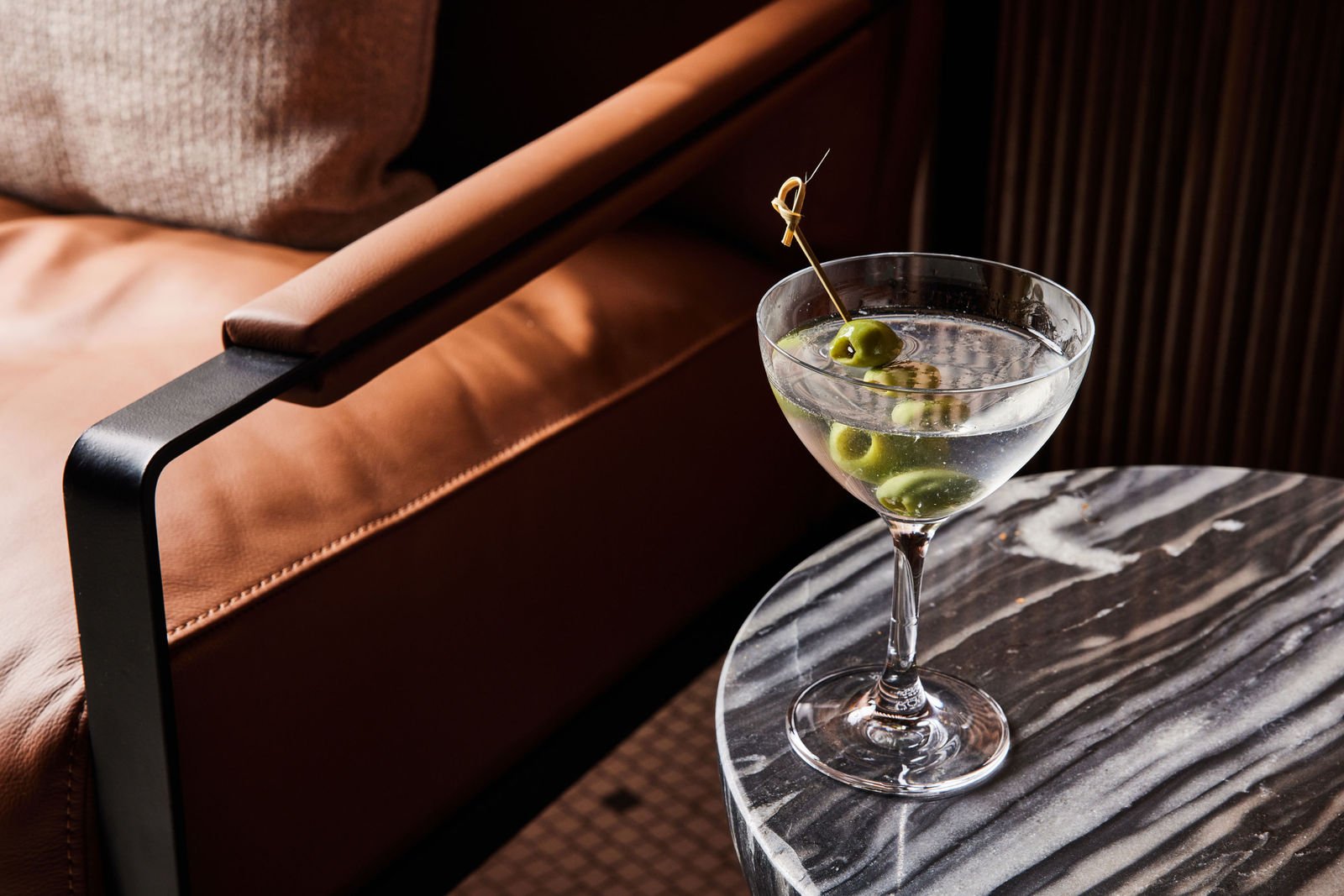 A dirty martini on a marble side table next to a leather chair