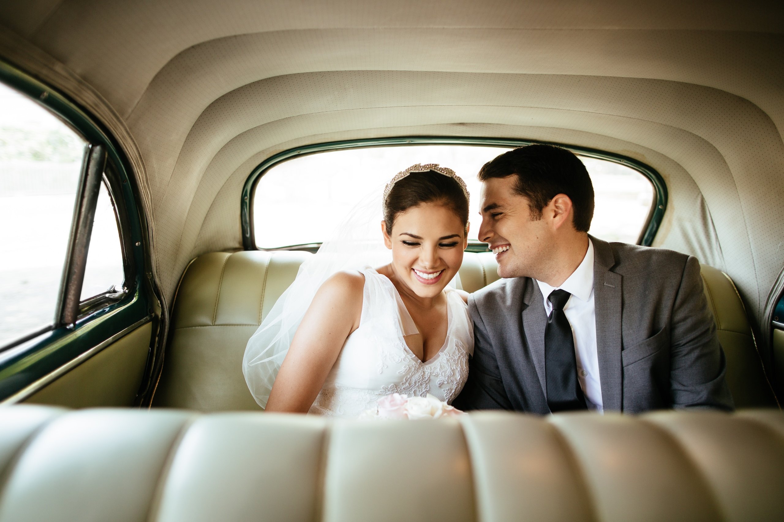 A newlywed couple laughing in the backseat of a classic car